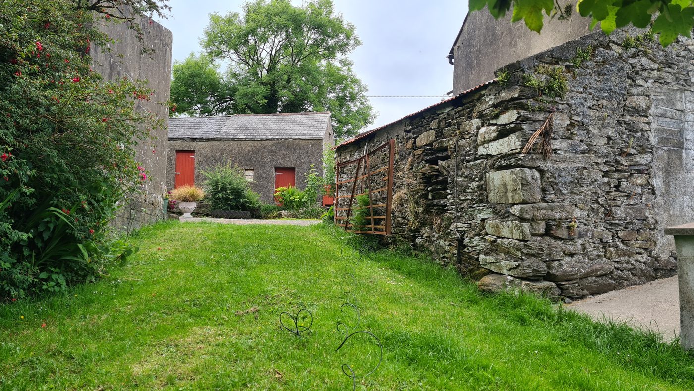 A cobbled farmhouse courtyard with red stable doors, a garden umbrella, picnic table and potted flowers