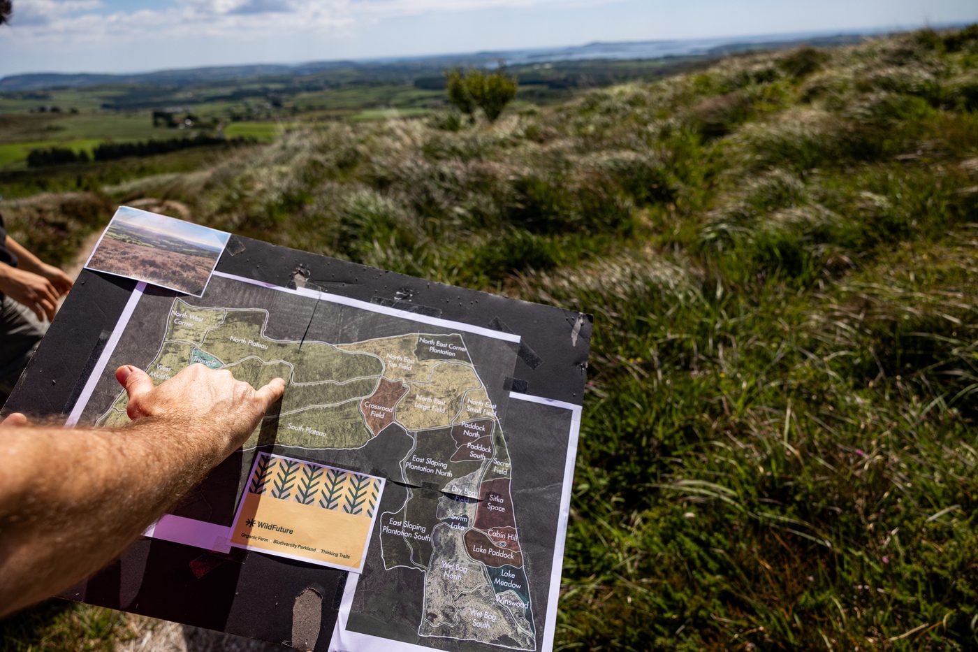 A hand pointing to a hand-drawn parcel map held against the hillside