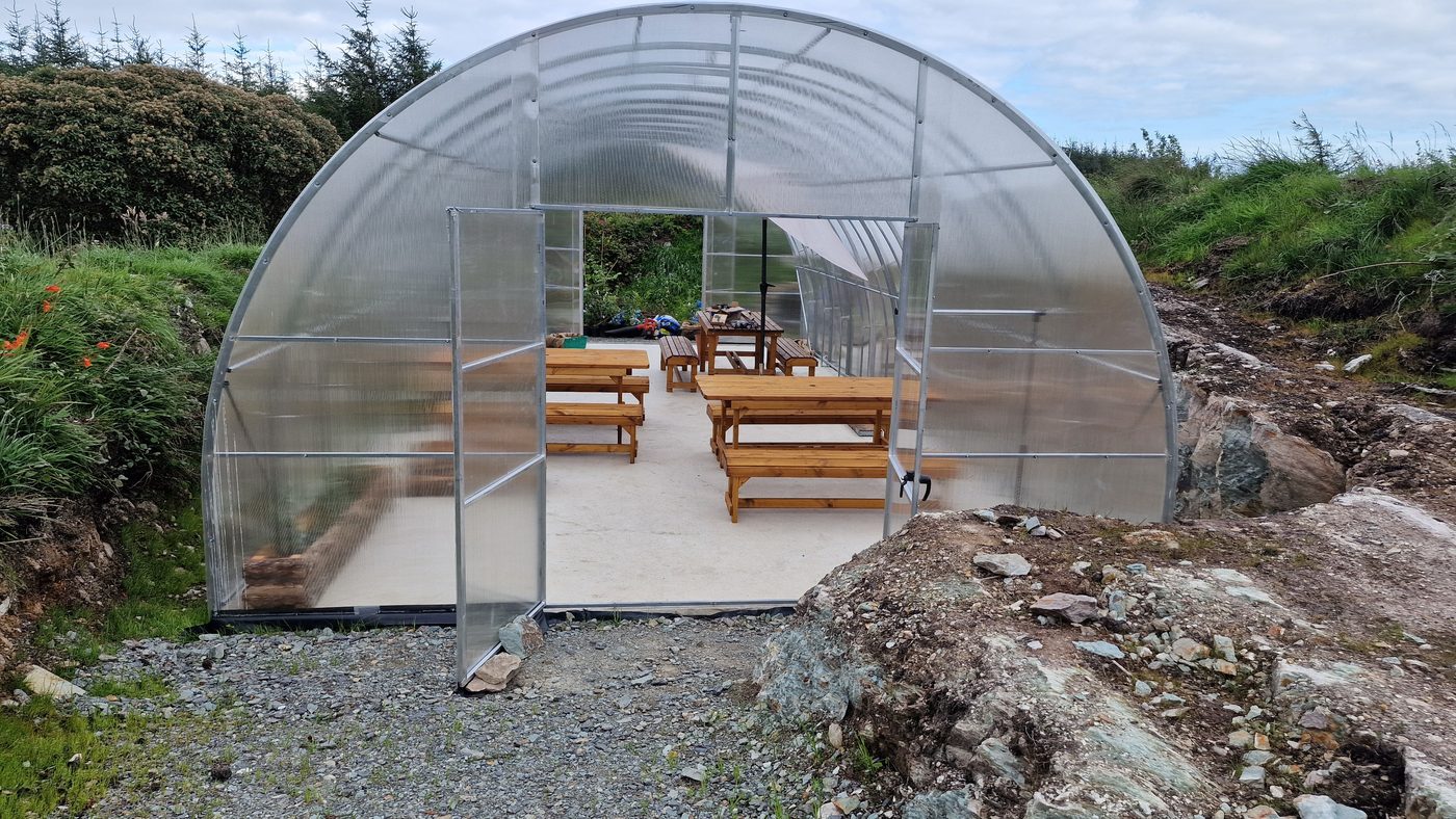 An open polytunnel workspace with timber benches, surrounded by hillside vegetation